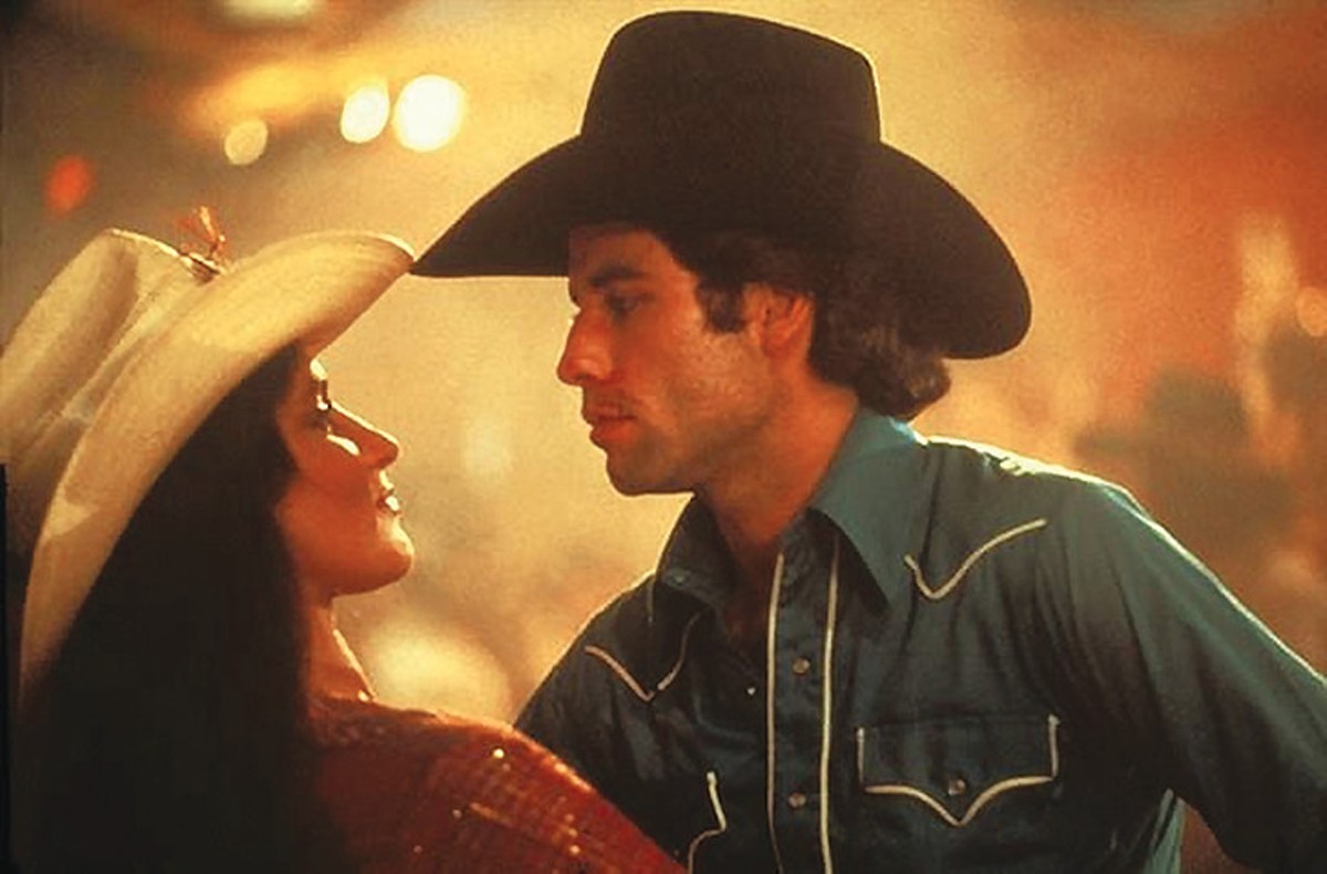Travolta boot scoots with revenge-in-a-cowboy-hat, Pam.