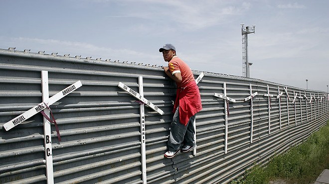 An aspiring migrant scales a fence to cross the U.S.-Mexico border.