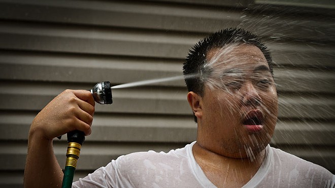 A man seeks relief from the heat by blasting himself in the face with a garden hose.