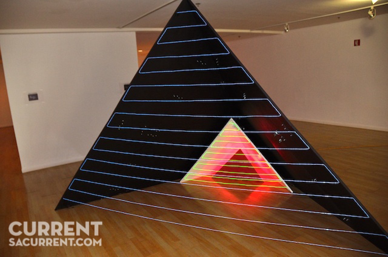 An eight-foot tall, three-sided pyramid by SA artist Jonathan Sims is covered with motifs that seem vaguely Sci-Fi, an interstellar language, perhaps. One of the sides is missing; lines of small lights describe the plane instead, allowing one to see inside a smaller triangle &#151; a pyramid within a pyramid. Secrets revealed to reveal, of course, more secrets.
