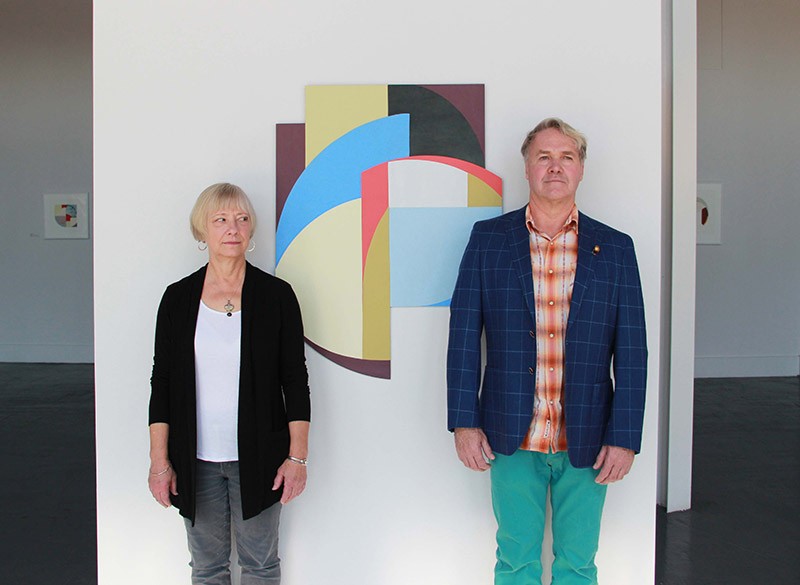Artists Constance Lowe and Gary Sweeney stand stiffly in front of one of Lowe’s geometric abstractions. - COURTESY