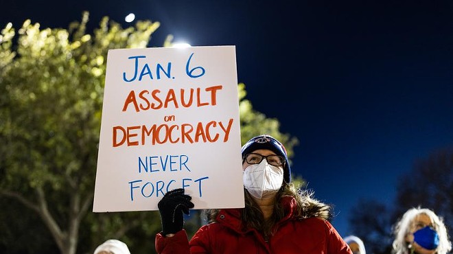A woman holds a sign at a candlelight vigil at the Texas Capitol on Jan. 6, 2022, to mourn the one-year anniversary of the attack on the U.S. Capitol.
