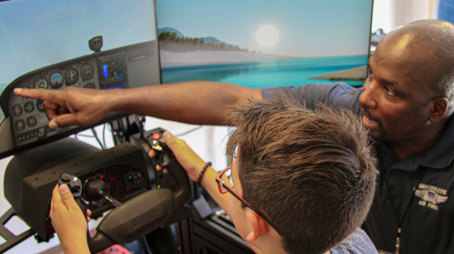 A flight simulator student sits while an instructor tells him what to do.