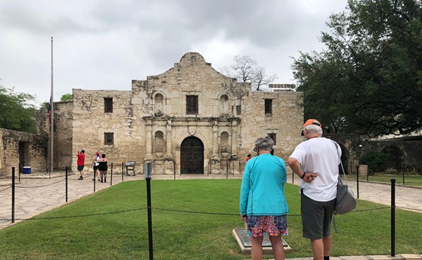 A man and woman read a sign at the  Alamo.