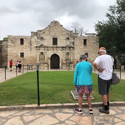 A man and woman read a sign at the  Alamo.
