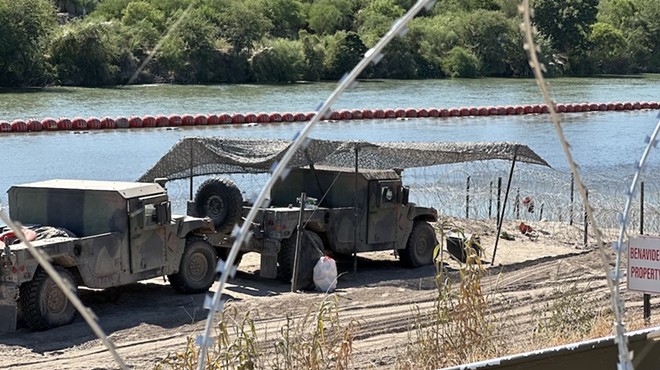 Military vehicles sit behind barbed wire barriers along the U.S.-Mexico border.