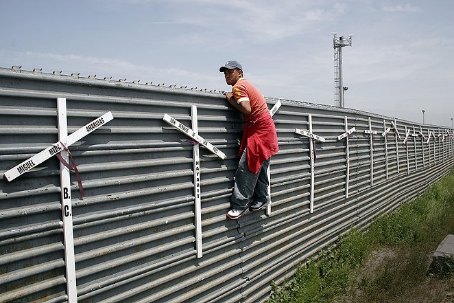An aspiring migrant scales a fence to cross the U.S.-Mexico border. - WIKIMEDIA COMMONS