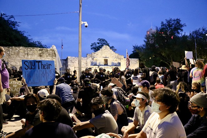 Anti-police brutality protestors sit down in front of the Alamo as armed TITFF members and police stand in the background. - JAMES DOBBINS