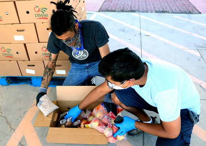 Volunteers Ashanti Williams (left), 30, and Saurau Majumdar, 29, sort through boxes of food at Eco Centro at San Antonio College on June 24. Each box contain apples, oranges, onions, potatoes, carrots and a pound of pinto beans. - ANDREA MORENO / HERON CONTRIBUTOR