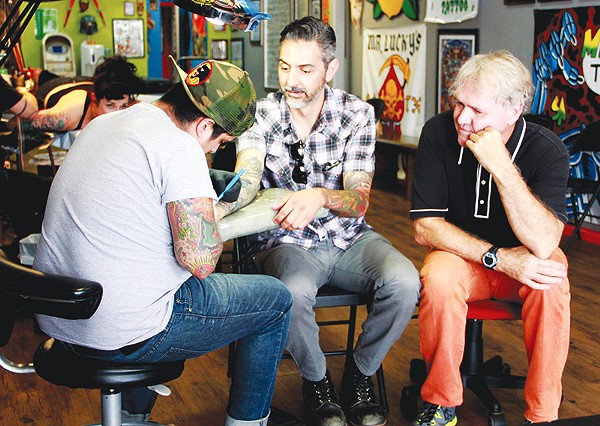 Steve Candelario of Mr. Luckys Tattoo does a tune up on Ricky Armendariz's arm as Gary Sweeney looks on. - COURTESY