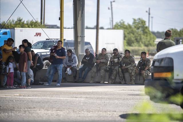 Members of the Texas National guard sit in the shade with people who were apprehended by state troopers. - Texas Tribune / Sergio Flores