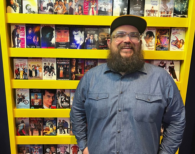 Be Kind & Rewind owner Alex Amaro stands in front of a display of VHS covers inside the bar. - Kiko Martinez