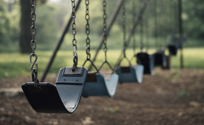 A playground swing set sits unused. - Unsplash / Aaron Burden