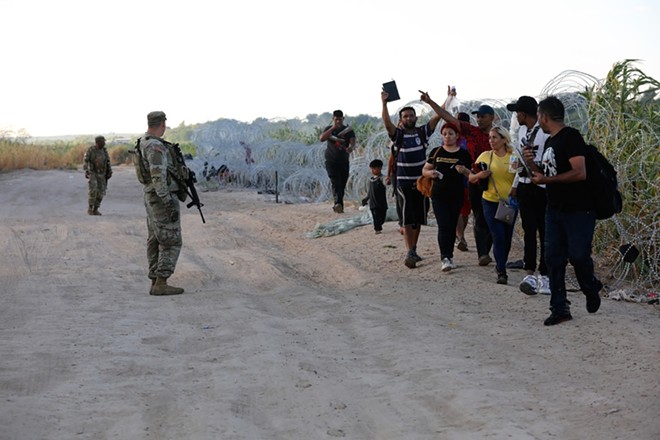A group of migrants seeking U.S. asylum crawl through razor wire on the banks of the Rio Grande River to enter the U.S. and turn themselves in to authorities. - Shutterstock / Vic Hinterlang