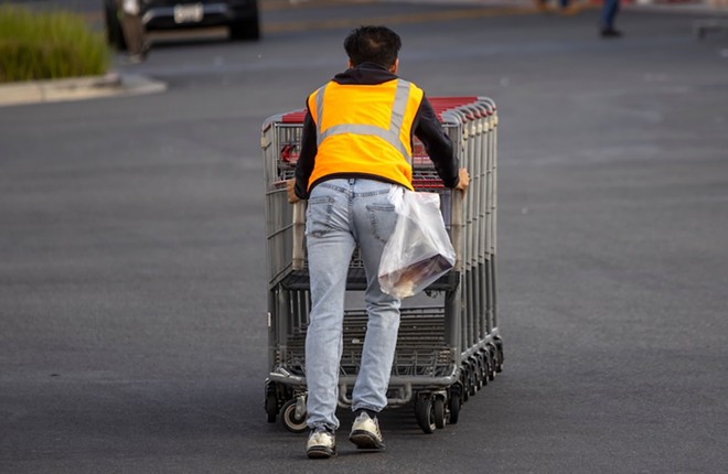 A grocery worker pushes carts through a parking lot. - Shutterstock / F Armstrong Photography