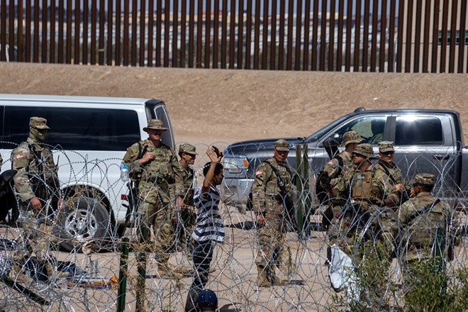 A man raises his hands in front of Texas National Guard troops after crossing the U.S.-Mexico border. - Shutterstock / David Peinado Romero