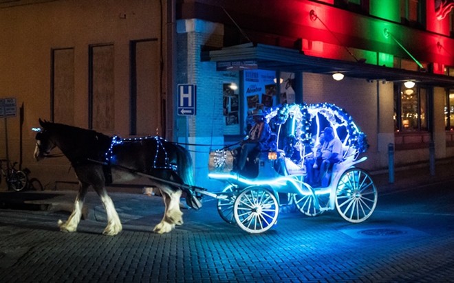 A horse and carriage carries tourists through the streets of San Antonio at night. - Shutterstock / NYCKellyWilliams