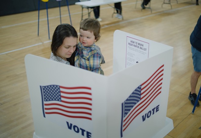 A woman holds her child while casting an election ballot. - Shutterstock / Frame Stock Footage