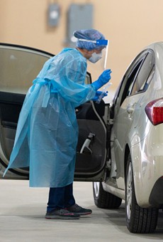 A worker at a drive-through testing facility in San Antonio prepares to collect a sample from someone in a vehicle.