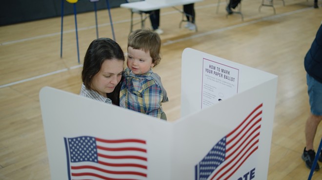 A woman holds her child while casting an election ballot.