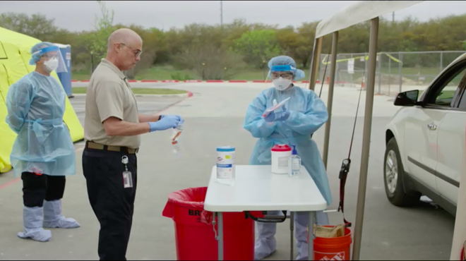 Emergency workers deal with a sample at a drive-through testing unit in a State of Texas-produced video.